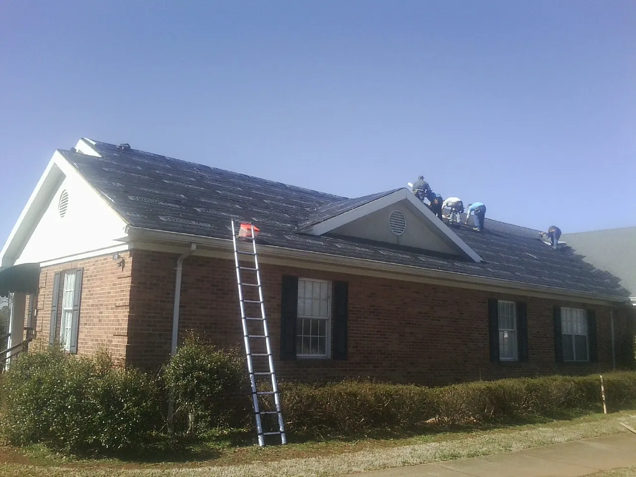 Crew tearing shingles off a brick ranch roof with a ladder set — Emergency Roof Repair work by our crew in Obion