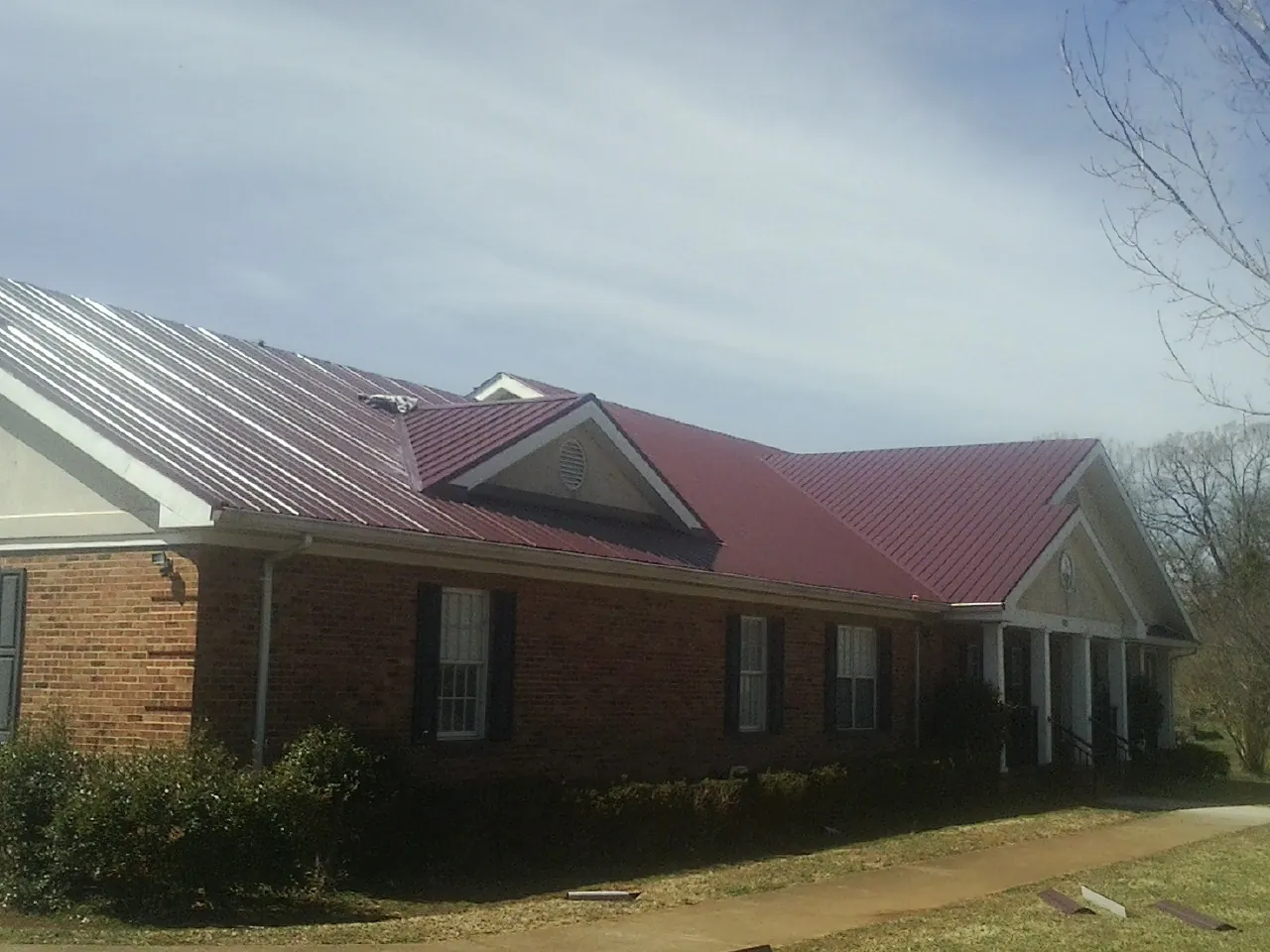 Red metal roof with gabled entries on a long brick building, from a Hail Damage Roof Repair job in Obion