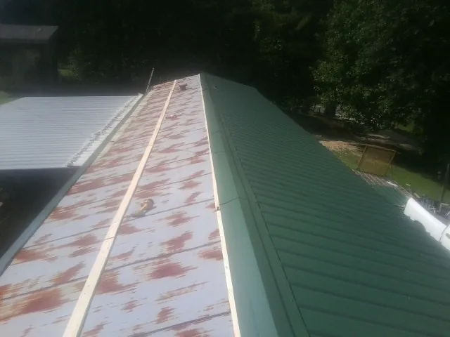 Old rusted panels beside newly installed green metal roofing — Wind Damage Roof Repair by Roofing Brothers in Obion