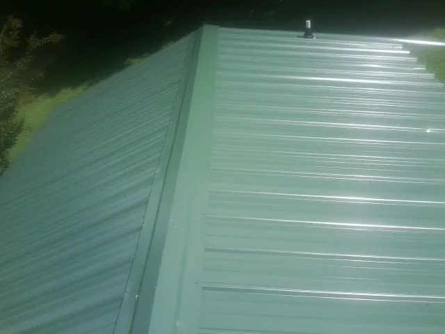 New green metal panels meeting at the ridge of a roof — Flat Roof Repair work by our crew in Obion
