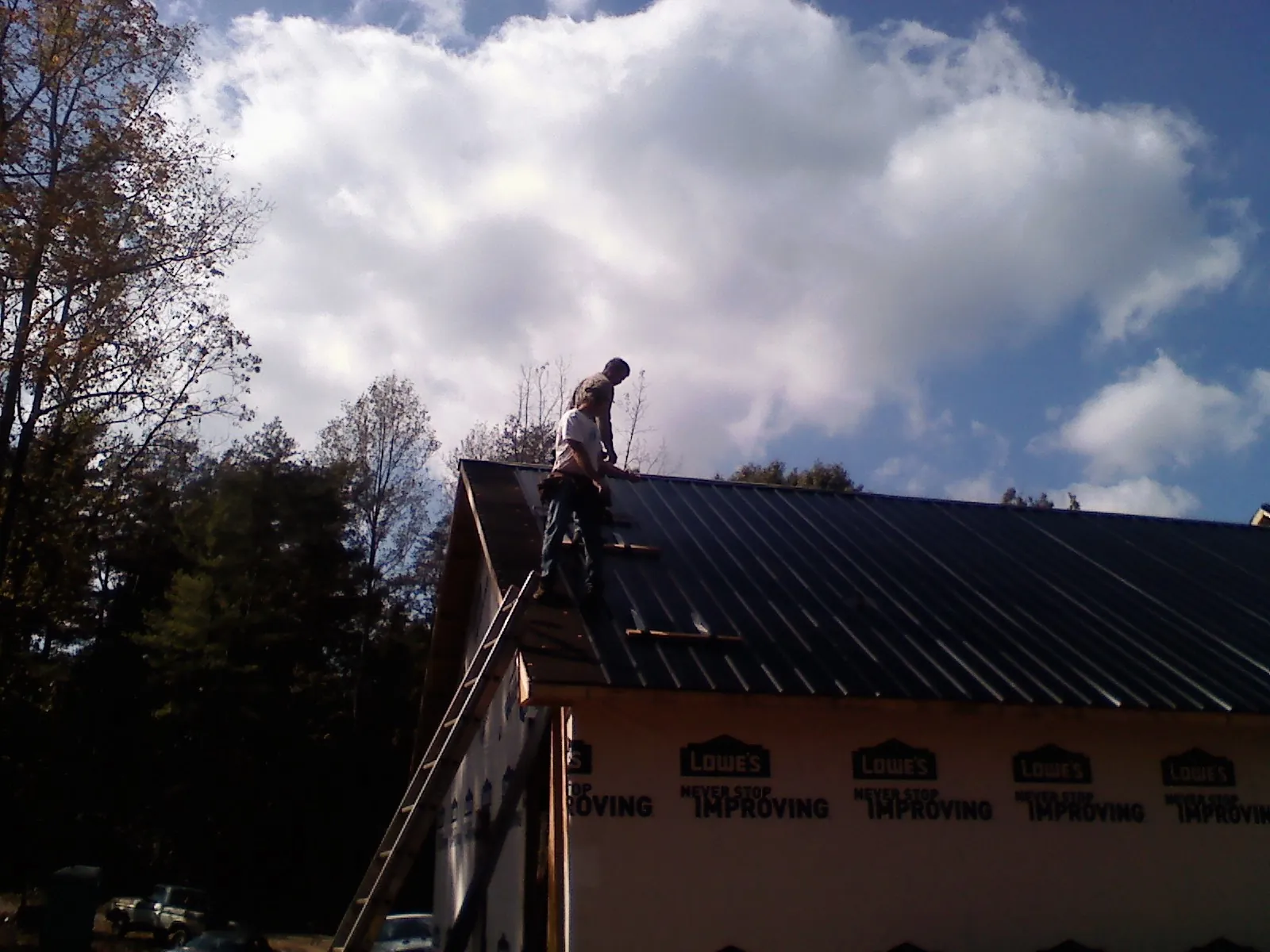 Roofer fastening dark metal panels high against a cloudy sky, from a Roof Inspection job in Obion