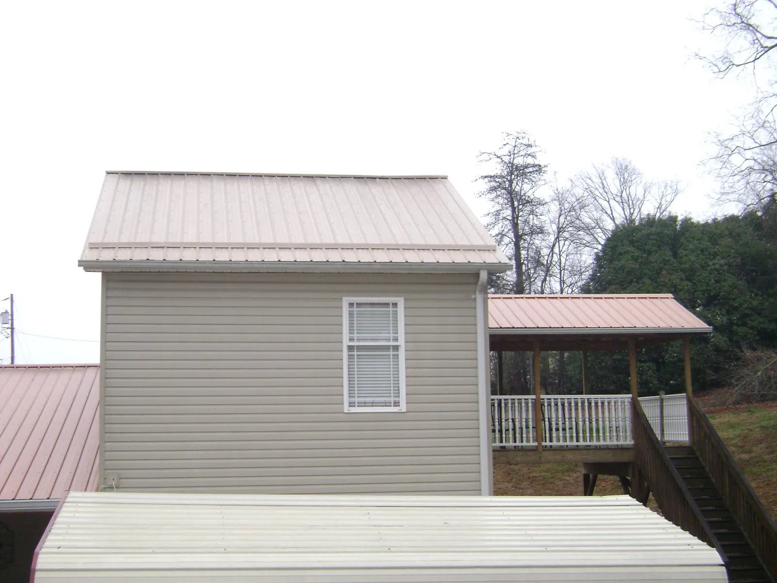 Tan metal roofs on a two story addition and attached porch, from a Roof Replacement job in Obion